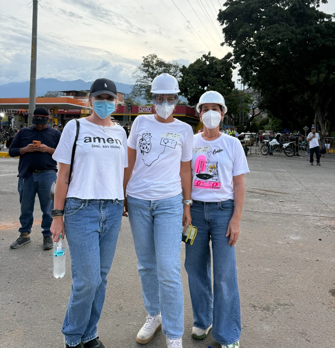 Tres personas con camisetas de AMEN y elementos de protección, juntas al aire libre.