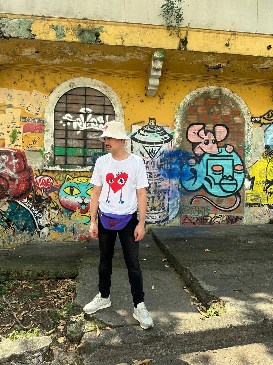 Camiseta blanca con un corazón rojo ilustrado, sombrero claro y canguro morado.