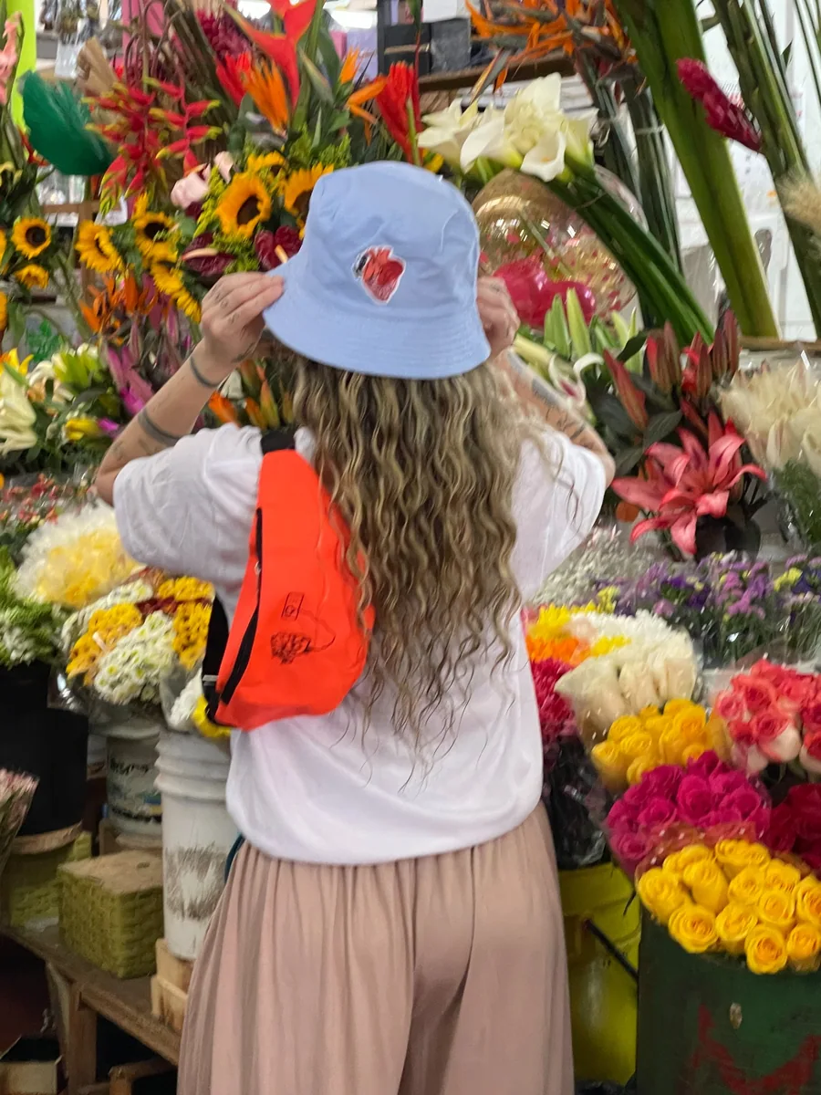 Sombrero azul con el corazón de AMEN y canguro naranja en un puesto de flores.